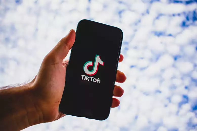 Mano de hombre sosteniendo teléfono celular con logo de TikTok en la pantalla.