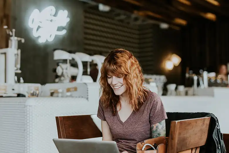 Mujer sonriendo mientras usa su laptop en lugar público
